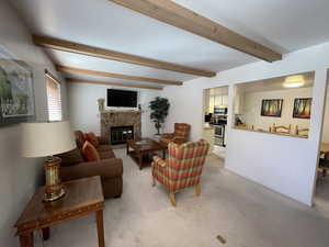 Living room with light carpet, beam ceiling, and a stone fireplace