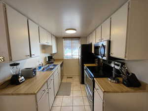 Kitchen with light tile patterned flooring, white cabinetry, sink, and appliances with stainless steel finishes