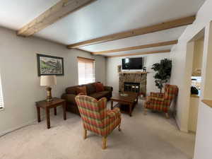 Carpeted living room with a stone fireplace and beamed ceiling