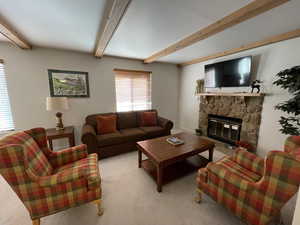 Carpeted living room featuring beam ceiling and a stone fireplace