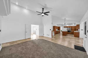 Unfurnished living room featuring light carpet, ceiling fan with notable chandelier, and high vaulted ceiling