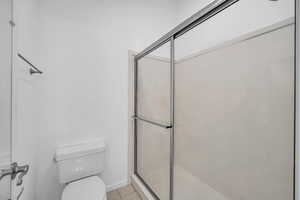 Bathroom featuring tile patterned flooring, toilet, and a shower with door