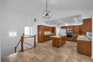 Kitchen with sink, a center island, an inviting chandelier, high vaulted ceiling, and appliances with stainless steel finishes