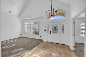 Carpeted foyer entrance featuring a notable chandelier and high vaulted ceiling