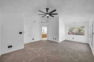 Interior space with a textured ceiling, ceiling fan, lofted ceiling, and carpet floors