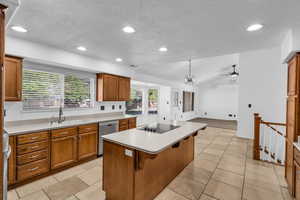 Kitchen with dishwasher, sink, black electric cooktop, a textured ceiling, and a kitchen island