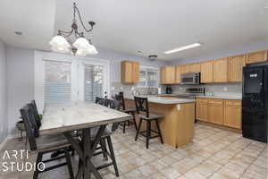 Kitchen with hanging light fixtures, an inviting chandelier, a breakfast bar area, light brown cabinetry, and appliances with stainless steel finishes