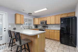 Kitchen featuring light brown cabinets, kitchen peninsula, sink, and appliances with stainless steel finishes