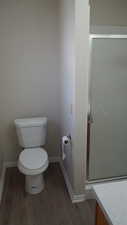 Bathroom featuring wood-type flooring, toilet, and a shower with door