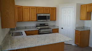 Kitchen featuring sink, light hardwood / wood-style flooring, light stone countertops, kitchen peninsula, and stainless steel appliances