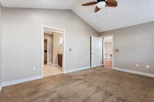 Unfurnished bedroom with connected bathroom, light carpet, ceiling fan, and lofted ceiling