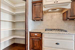 Kitchen featuring decorative backsplash, light stone countertops, wood-type flooring, and stainless steel gas cooktop