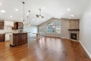 Kitchen featuring pendant lighting, lofted ceiling, dark wood-type flooring, a stone fireplace, and appliances with stainless steel finishes