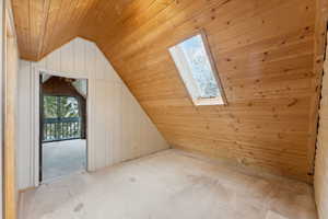 Additional living space featuring vaulted ceiling with skylight, wood walls, light colored carpet, and wood ceiling