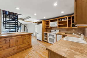 Kitchen featuring light wood-type flooring, tasteful backsplash, white appliances, sink, and tile countertops