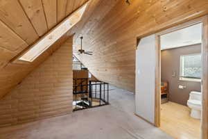 Bonus room featuring wood walls, vaulted ceiling with skylight, ceiling fan, wood ceiling, and brick wall