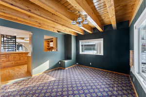 Carpeted empty room with beamed ceiling, wooden ceiling, and a notable chandelier