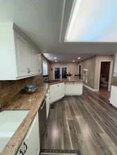 Kitchen with white cabinets, light stone countertops, kitchen peninsula, and dark wood-type flooring