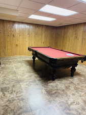 Recreation room featuring wooden walls, a drop ceiling, and pool table