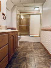 Full bathroom featuring shower / bath combination with glass door, a drop ceiling, vanity, and toilet