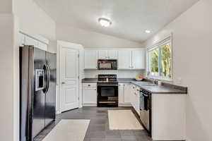 Kitchen with sink, white cabinets, black appliances, and vaulted ceiling