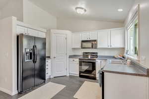 Kitchen featuring vaulted ceiling, sink, black appliances, dark tile patterned flooring, and white cabinets