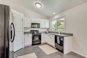 Kitchen with white cabinetry, sink, black appliances, and lofted ceiling