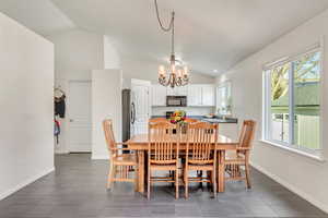 Dining space featuring dark tile patterned flooring, vaulted ceiling, and a notable chandelier