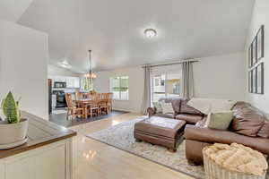 Living room with light hardwood / wood-style flooring, lofted ceiling, and an inviting chandelier