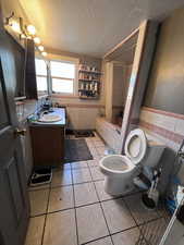 Full bathroom with tile patterned floors, shower / bath combo, a textured ceiling, and tile walls