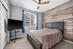 Bedroom with ceiling fan, light carpet, wooden walls, and a closet