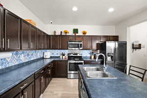 Kitchen with sink, stainless steel appliances, a textured ceiling, decorative backsplash, and light wood-type flooring