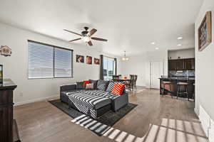 Living room featuring ceiling fan with notable chandelier and light wood-type flooring