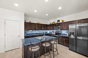 Kitchen with sink, a center island with sink, stainless steel appliances, and light hardwood / wood-style floors