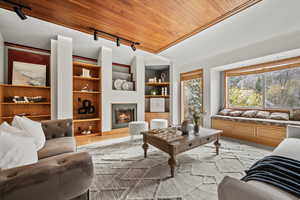 Living room with rail lighting, ornamental molding, built in features, wooden ceiling, and light hardwood / wood-style floors