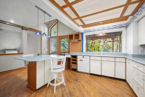 Kitchen featuring white cabinetry, dishwasher, light hardwood / wood-style flooring, decorative light fixtures, and a breakfast bar