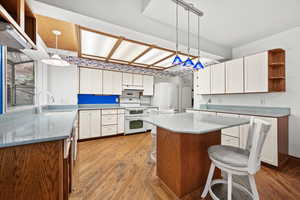 Kitchen with a kitchen bar, white appliances, sink, light hardwood / wood-style flooring, and white cabinetry