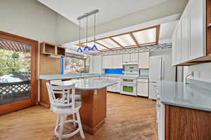 Kitchen with a center island, light hardwood / wood-style floors, decorative light fixtures, white appliances, and white cabinets