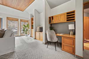 Office space featuring wooden ceiling, light colored carpet, built in desk, and lofted ceiling