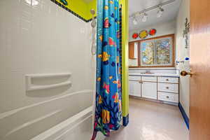 Bathroom with vanity, shower / bathtub combination with curtain, and track lighting