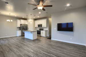 Kitchen featuring white cabinetry, dark hardwood / wood-style flooring, an island with sink, pendant lighting, and appliances with stainless steel finishes