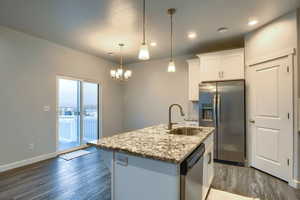 Kitchen featuring appliances with stainless steel finishes, sink, decorative light fixtures, white cabinetry, and an island with sink