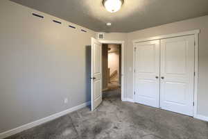 Unfurnished bedroom with light carpet, a textured ceiling, and a closet