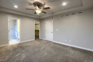 Unfurnished bedroom featuring carpet flooring, a walk in closet, a tray ceiling, and ceiling fan