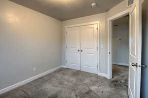 Unfurnished bedroom featuring a textured ceiling, light carpet, and a closet