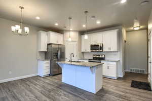 Kitchen with appliances with stainless steel finishes, sink, a center island with sink, hardwood / wood-style flooring, and white cabinets