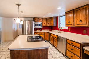 Kitchen with a kitchen island, sink, stainless steel appliances, and hanging light fixtures