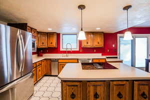 Kitchen with sink, pendant lighting, a textured ceiling, a kitchen island, and appliances with stainless steel finishes