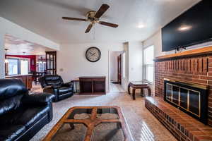 Carpeted living room with ceiling fan, a textured ceiling, and a brick fireplace