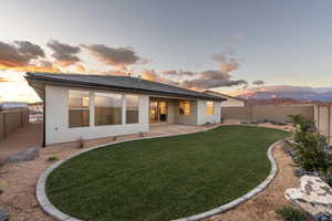 Back house at dusk featuring a mountain view, a patio area, and a lawn